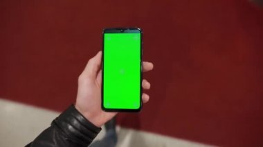 Pov, alışveriş merkezinde yeşil ekranlı akıllı telefon tutan erkek.