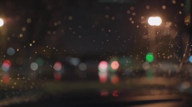 Ön cam sileceği ile temizlenen yağmur damlalarıyla ön araba penceresinin arka planı