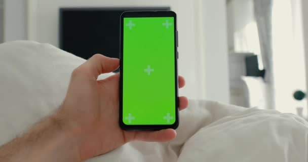 POV, mão masculina segurando smartphone com tela verde em uma cama — Vídeo de Stock