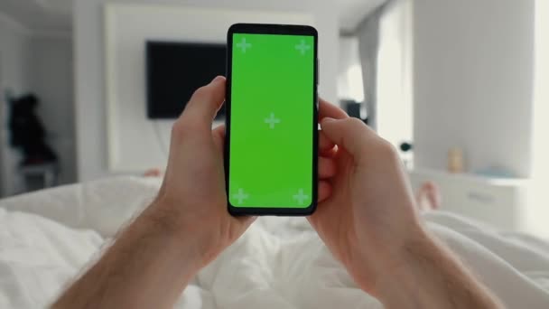 Pov，男性手持智能手机，床上有绿色屏风 — 图库视频影像