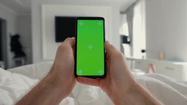 POV, mão masculina segurando smartphone com tela verde em uma cama — Vídeo de Stock