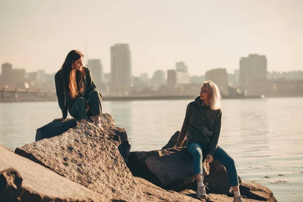 Silueta dvou mladých žen sedících na kamenech u řeky — Stock fotografie