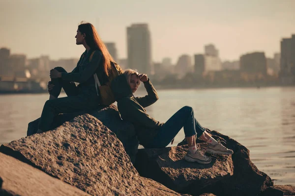 Silhouette of two young women sitting on stones near river — Stock Photo, Image