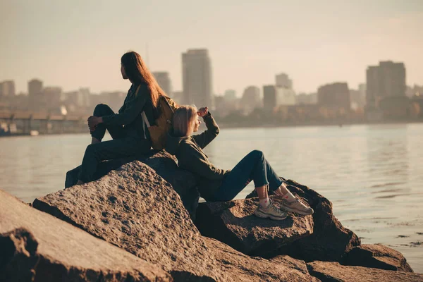 Silueta de dos jóvenes sentadas sobre piedras cerca del río —  Fotos de Stock