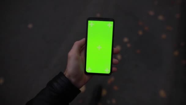 Pov αρσενικό χέρι κρατώντας πράσινη οθόνη mockup του smartphone στέκεται στο δρόμο της πόλης νύχτα — Αρχείο Βίντεο