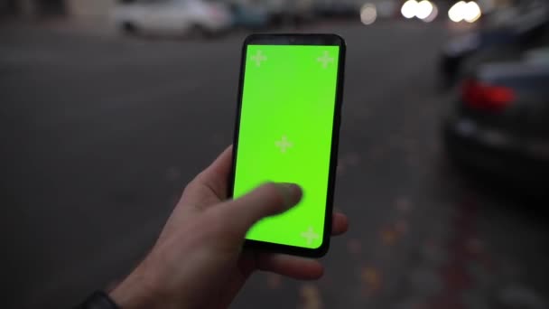 Pov fiatal férfi használ zöld képernyő mockup okostelefon álló éjszakai városi közlekedési utcán — Stock videók
