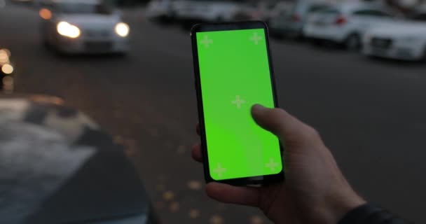 POV nuori mies käyttää vihreää näyttöä mallinnus älypuhelimen seisoo yöllä kaupungin liikenteen kadulla — kuvapankkivideo