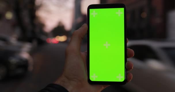 Мужчина держит в руке макет смартфона с зеленым экраном, идущего по ночной городской улице — стоковое видео