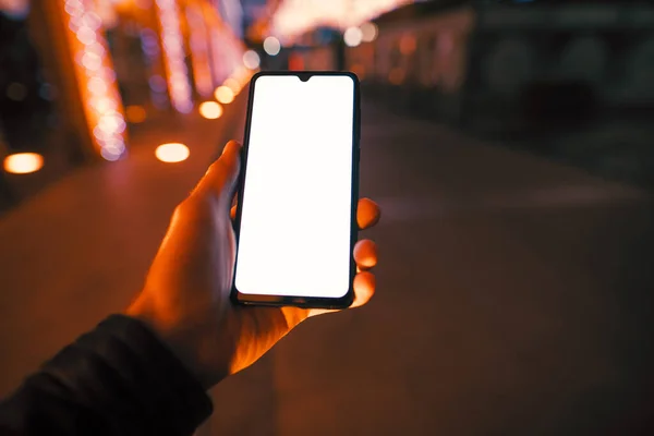 夜市男性手持带有空白显示屏的智能手机 — 图库照片