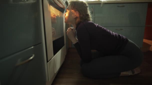 Женщина ждет, пока выпечка готовится в духовке — стоковое видео