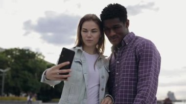 İki çok ırklı arkadaş akıllı telefondan selfie çekiyor.