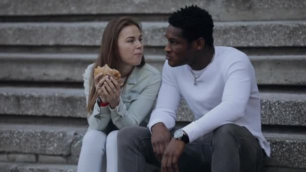 Mujer caucásica comiendo con su amigo africano en una ciudad — Vídeos de Stock