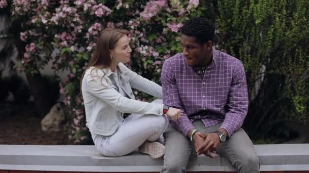 Két multiracionális barát ül a kerítésen és beszél a városban. — Stock videók