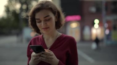 Şehir caddesinde yürürken akıllı telefonla mesajlaşan bir kadın.