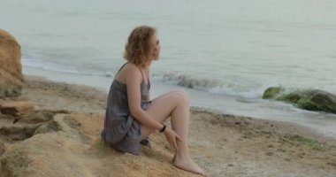Deniz kıyısında oturan aptal elbiseli mutlu kadın.