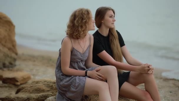 Dos amigas sentadas en piedra en la playa de mar — Vídeos de Stock