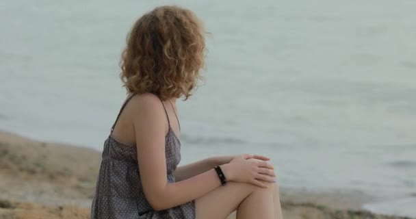 Vrouw in jurk ontspannen zitten op een zee strand — Stockvideo