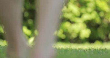 Çıplak ayaklı erkek bacakları çimenlerde yürür.