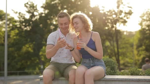 Junges Paar trinkt Saft im Park und liest Zutaten — Stockvideo