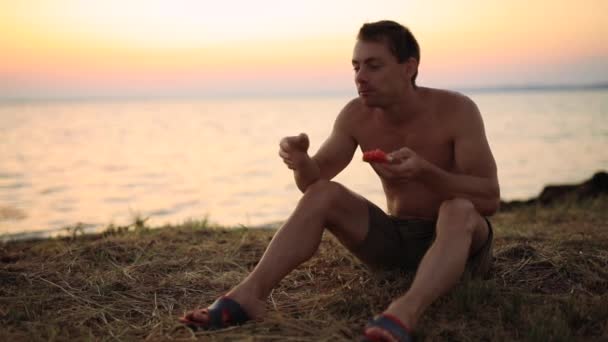 Funny man eating watermelon sitting near sea — Stock Video