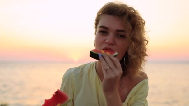 美しい女性は海の近くに座ってスイカを食べる — ストック動画