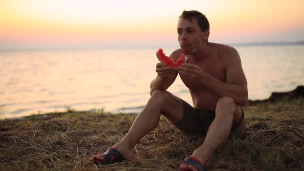 바다 근처에 앉아 수박을 먹고 있는 사람 — 비디오