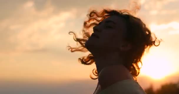 Silhueta de mulher encaracolada contra o pôr-do-sol laranja fundo — Vídeo de Stock