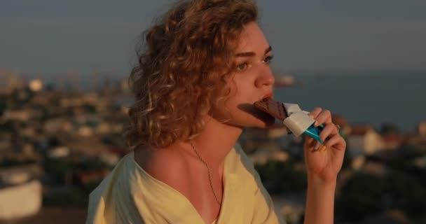 Mulher encaracolada comendo chocolate acima da cidade — Vídeo de Stock