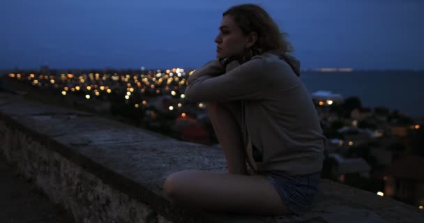 Kvinde afslappende sidder på toppen over byen om aftenen – Stock-video