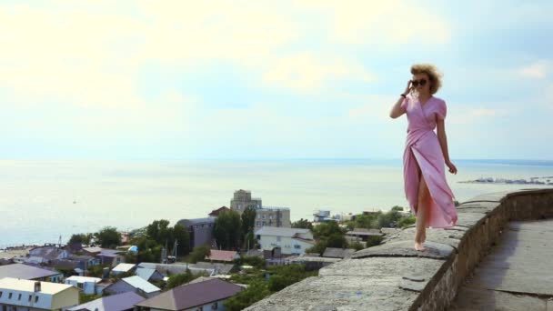 Mulher em um vestido rosa caminha ao longo do terraço contra o fundo do mar — Vídeo de Stock