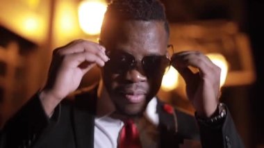 Siyah giysili Afrikalı adam gece şehrinde güneş gözlüğü takıyor.