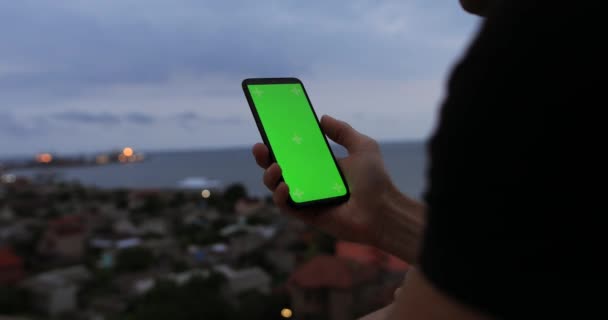 Mano masculina sosteniendo teléfono inteligente con pantalla vacía en el mar de la noche — Vídeos de Stock