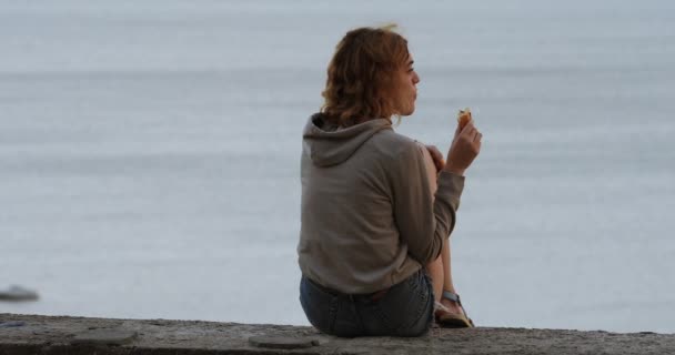 Lockig kvinna äter croissant mot havet bakgrund — Stockvideo