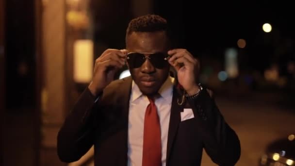 Afrikansk man i svart kläder mörka solglasögon i natten staden — Stockvideo