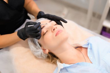 Güzellik uzmanı, güzellik salonunda sivilce temizleme kaşığı kullanarak müşterileri yüz yüze getiriyor.