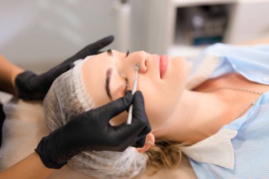 Güzellik uzmanı, güzellik salonunda sivilce temizleme kaşığı kullanarak müşterileri yüz yüze getiriyor.