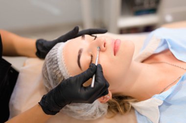 Güzellik uzmanı, güzellik salonunda sivilce temizleme kaşığı kullanarak müşterileri yüz yüze getiriyor.