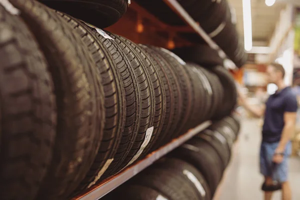 Hombre elige neumáticos de coche en un escaparate —  Fotos de Stock