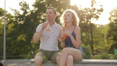 Genç çift parkta meyve suyu içiyor.