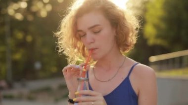 Parkta meyve suyu içen genç bir kadın