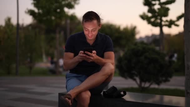 공원에서 해변에 앉아 휴대 전화를 사용하는 남자 — 비디오