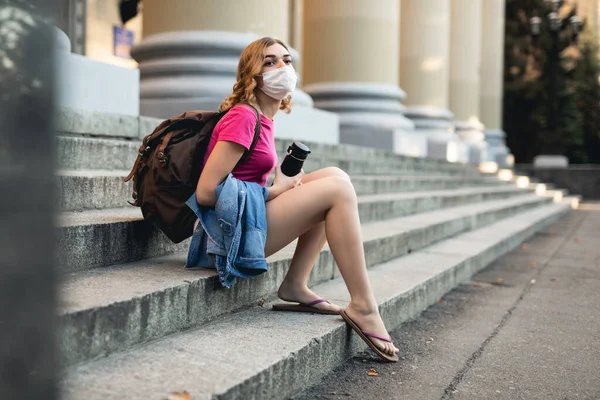 Student kobieta w masce chirurgicznej twarzy siedzi w pobliżu uniwersytetu — Zdjęcie stockowe