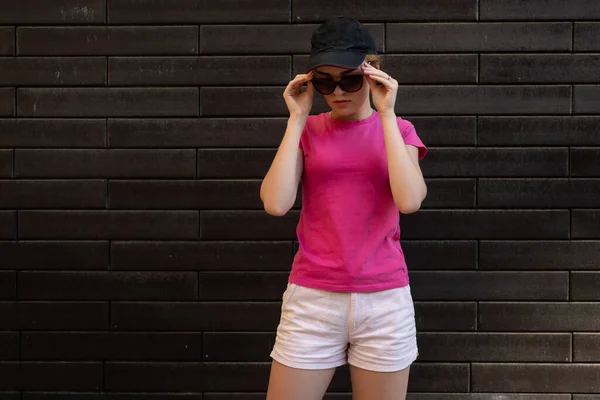 Vacker kvinna i blank rosa t-shirt stående mot tegelvägg — Stockfoto