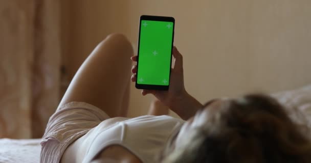 ベッドの上に横たわるスマートフォンの緑の画面を使用して女性のモックアップ — ストック動画