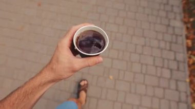POV, adam sonbahar sokağı boyunca kağıt kahve fincanı taşıyor.