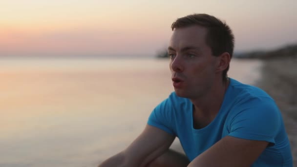 Mężczyzna ciężko oddycha siedząc na plaży morskiej — Wideo stockowe