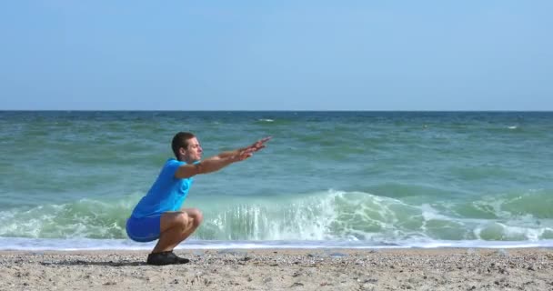 Jongeman doet squats oefening op het strand van de oceaan — Stockvideo