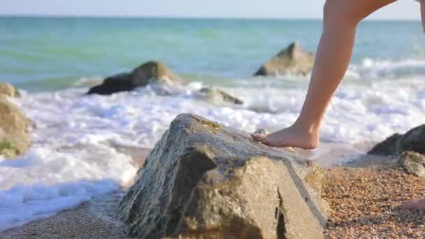 Vrouwelijke benen in jurk staande op grote steen in de buurt van zee strand — Stockvideo
