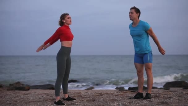Pareja joven haciendo sentadillas ejercicio en la playa del océano en cámara lenta — Vídeos de Stock