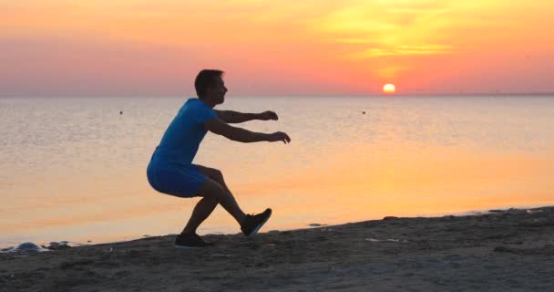 Giovane uomo che fa squat su una gamba alla spiaggia del mare — Video Stock